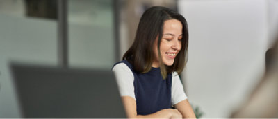 茶色のロングヘアの女性が、屋内環境で座って笑顔を見せながら下を見ている。