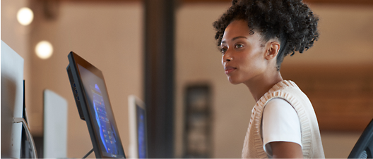 在現代化的辦公室場景中，一名年輕女性在配有電腦螢幕的立式辦公桌前專心工作。