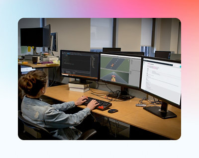 A female software developer working at a multi-monitor setup in an office, coding and debugging software.