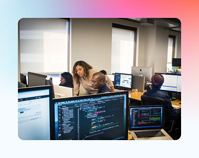 Diverse group of professionals working on computers in an office environment, focusing on screens with various code and data visible.