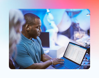 Man reviewing data on a laptop in a busy office setting with colleagues surrounding him.