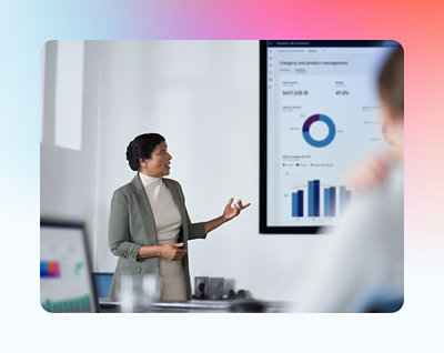 A professional woman presents financial data on a screen to her audience in a modern office setting.