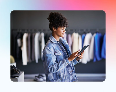 A woman in a denim jacket is using a tablet in a clothing store