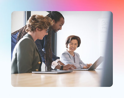 Three professionals, one with dreadlocks, sitting around a laptop in a meeting room, discussing work contentedly.