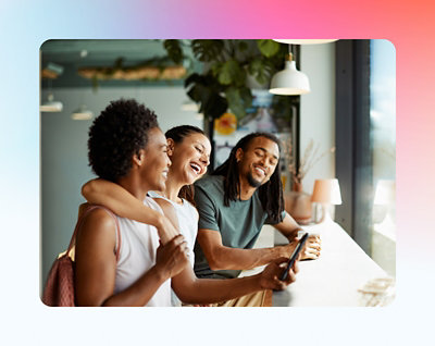 Three friends laughing and looking at a smartphone together in a modern café.