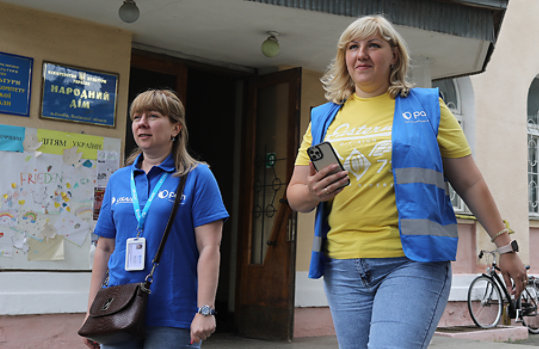Two Humanitarian Action workers wearing vests and lanyards coordinate aid to displaced Ukranians.