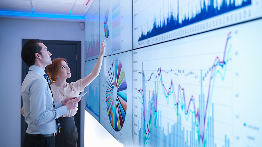 A person pointing at a large screen with graphs