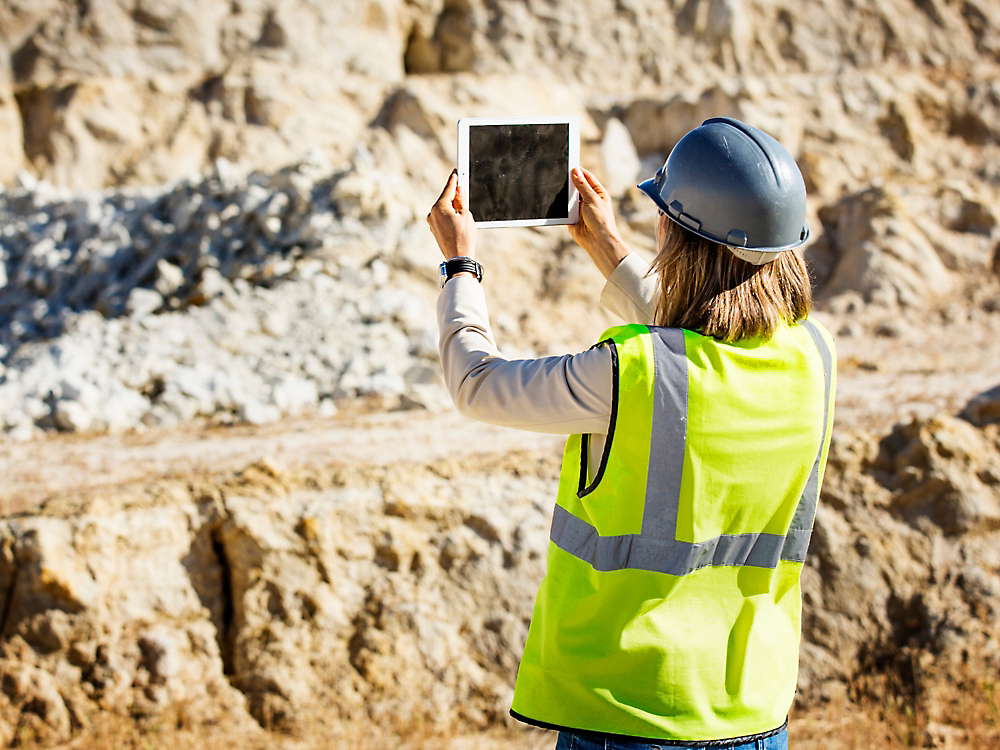 A person in a safety vest and hardhat holding a tablet