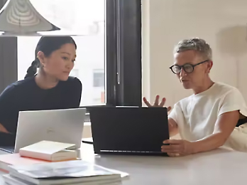 Zwei Personen sitzen, schauen sich einen Laptop an und diskutieren über ein Thema.