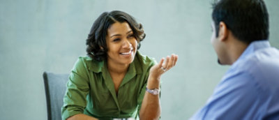Woman in green shirt smiling and talking to a man at a table during a casual meeting.