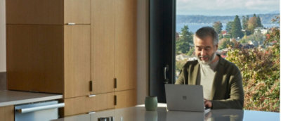 A man working on a laptop at a sleek kitchen counter with a scenic lake view in the background.