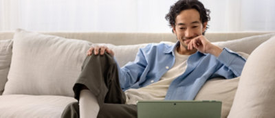 Man sitting on a sofa using a laptop, smiling and looking at the screen.