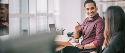 A man in a wheelchair smiles while discussing with a colleague in an office setting.