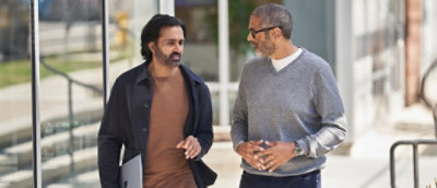 Two men in casual business attire walking and talking together outside an office building.