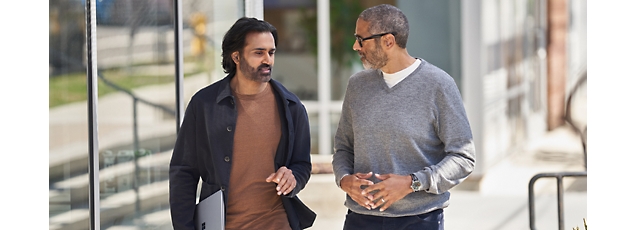 Two men in casual business attire walking and talking together outside an office building.