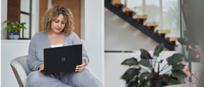 Professional woman with curly hair working on a laptop in a modern indoor setting with plants.