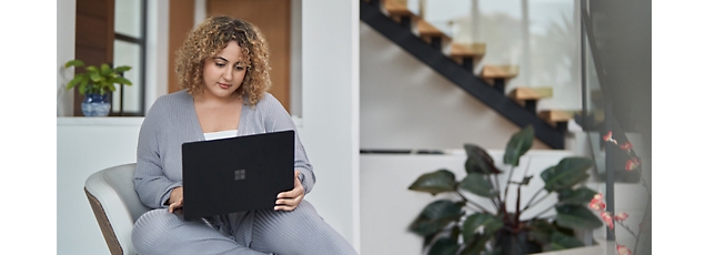 Professional woman with curly hair working on a laptop in a modern indoor setting with plants.