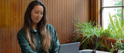 A woman in a green top smiles while using a computer in an office setting.