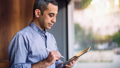A person in a blue shirt is standing indoors, holding a pen and a tablet.