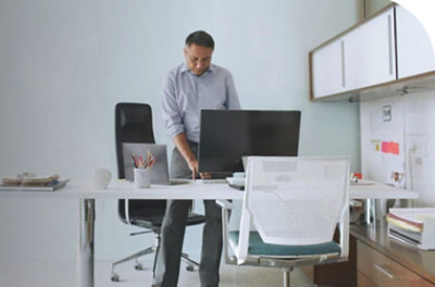 A person standing at a desk looking at a desktop monitor