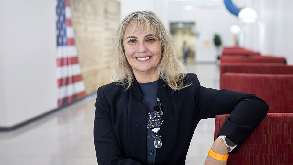 A woman smiling in a hallway with an American flag.