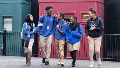 Five students laughing and talking outside a building.