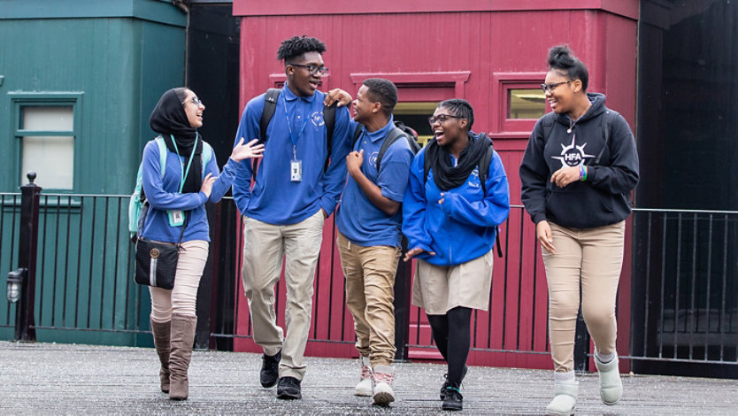 Five students laughing and talking outside a building.