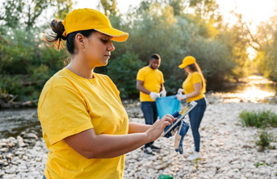 People in yellow shirts and hats participating in a cleanup activity by a river.