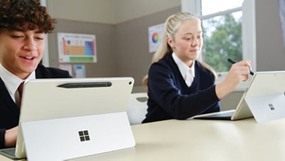 Two students seated side by side in a classroom, using a Surface Pro 12" Platinum device in laptop mode.