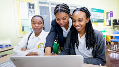 Three students engaged with a laptop in a classroom.