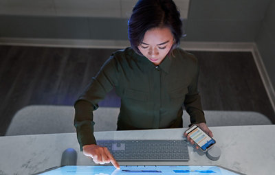 A person using a large touchscreen monitor and holding a mobile phone.