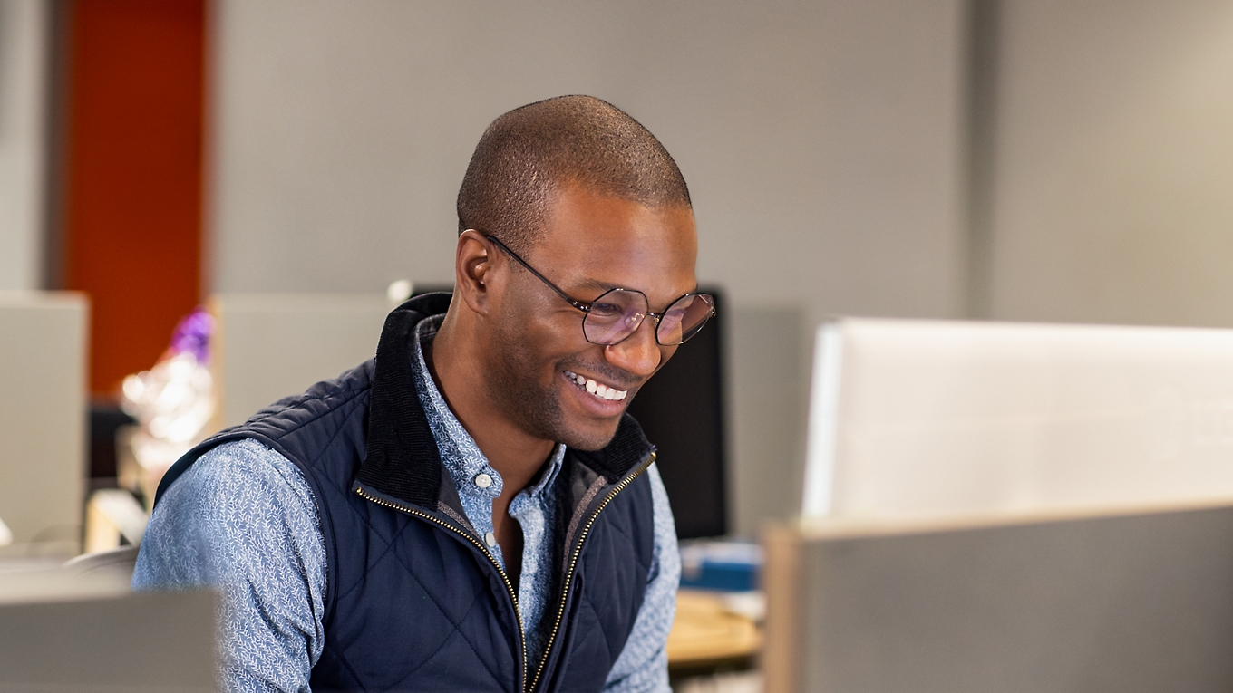 En person som sitter på kontoret og smiler og jobber med en bærbar datamaskin