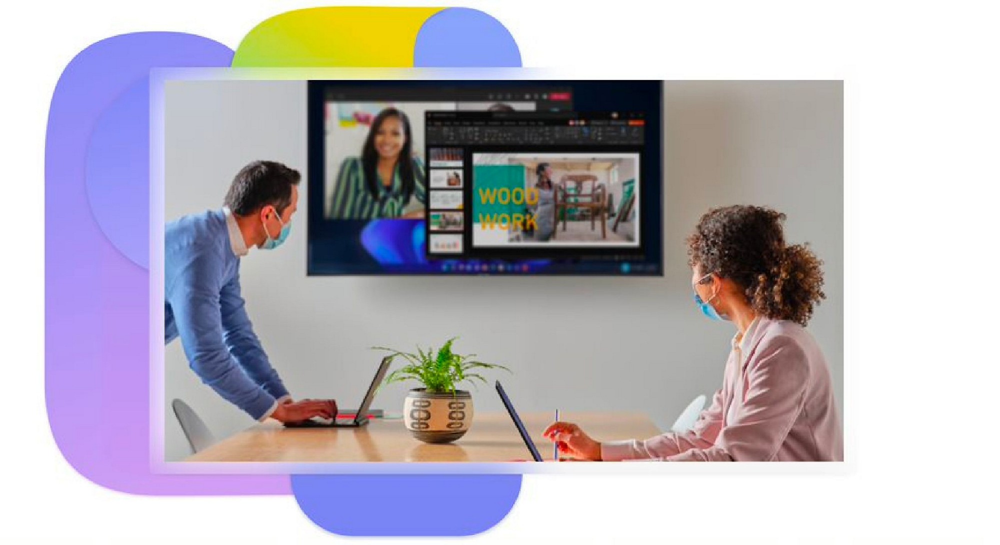 Dos personas en una sala de reuniones que están usando portátiles y mirando una pantalla en la pared que muestra una videollamada de Teams y una presentación.