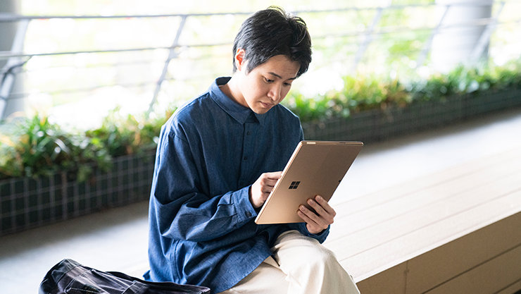 男性が外のベンチで Surface を縦にして操作している