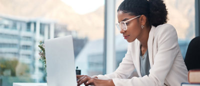 Una mujer trabaja con un portátil frente a una ventana.