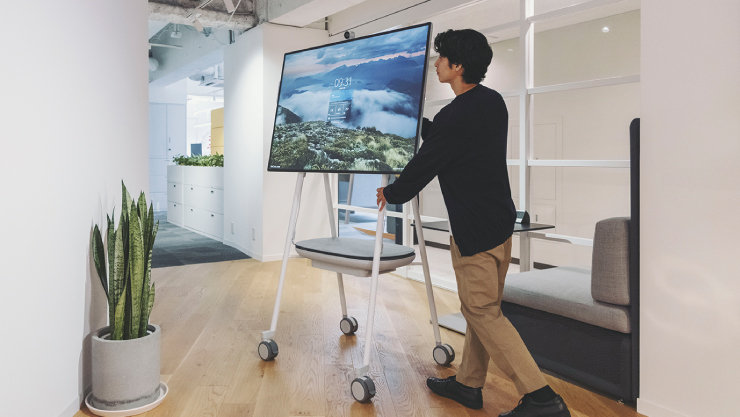 男性がキャスターのついている台に設置しているSurface Hub 3を運んでいる