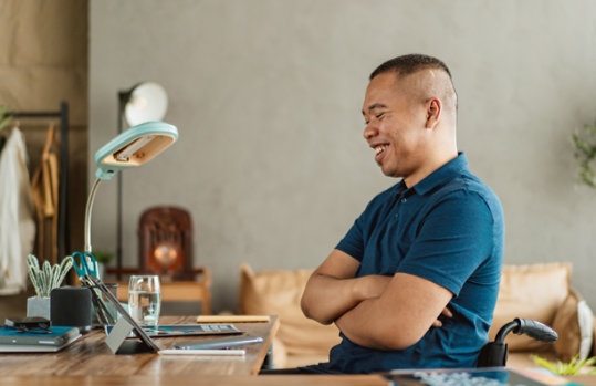 A person in a wheelchair smiles as he enjoys watching a video on a Surface device.