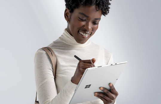 A smiling person uses Surface Slim Pen 2 on Surface Pro 8.