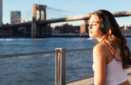 A woman listening with the the J B L Tune 760 N C Wireless Noise Cancelling Headphones in Black.