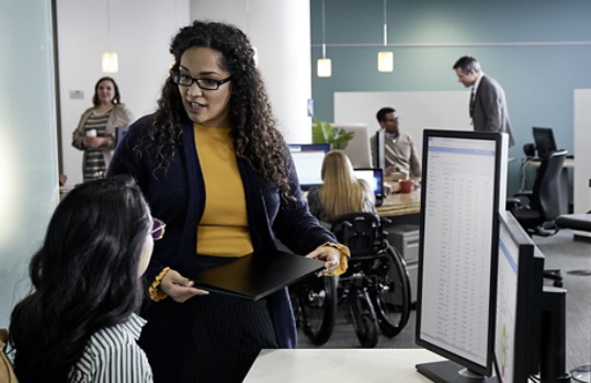 Mulher usando um dispositivo Surface com colega no trabalho.