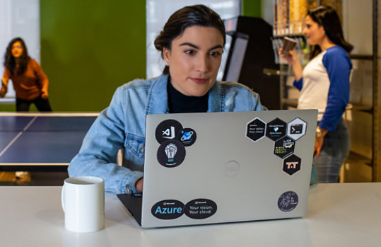 A woman works on her laptop, which is decorated with Azure-themed stickers. 