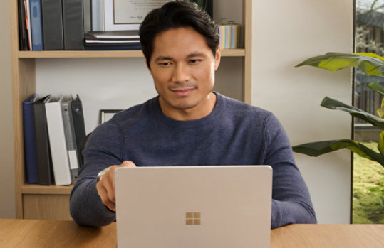 A man sitting at a desk using a Platinum 13 inch Surface Laptop.