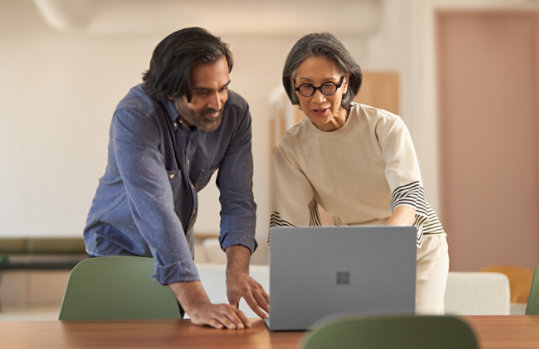 Two coworkers look at something on a Surface Laptop.