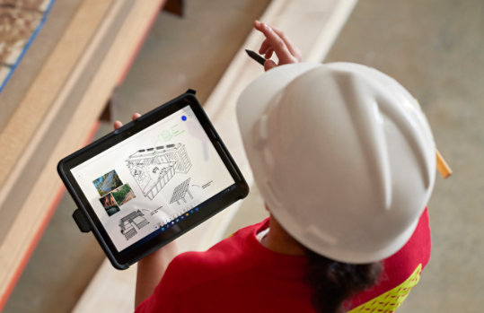 Une femme arbore un casque de sécurité en utilisant une Surface Go 3 sur un chantier.