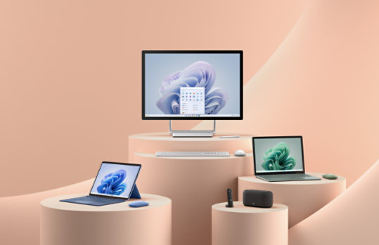A display of several Surface devices and tech accessories on a peachy-pink background.