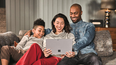 A family, sitting on a couch, using a Surface laptop together.