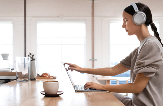 Osoba nosząca słuchawki Surface Headphones, pracująca na laptopie.
