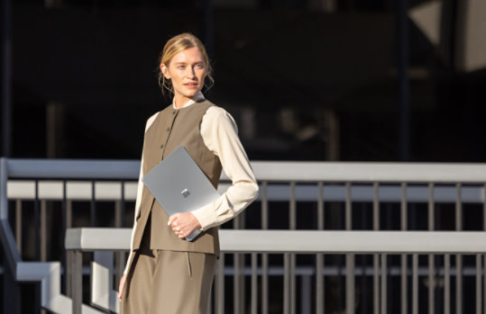 A person holds a 13.8-inch Surface Laptop for Business with 5G while crossing the street, suggesting the device's secure design even in public settings. 