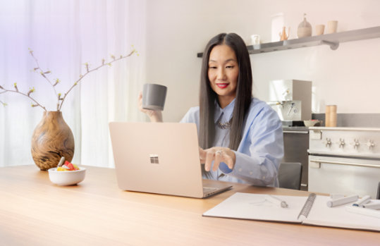 Une personne assise à une table de cuisine, tenant une tasse, utilisant un Dune Surface Laptop.