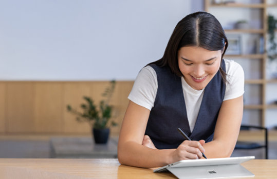 Henkilö käyttää Surface Pro yrityksille neuvottelupöydän ääressä Surface Slim -kynällä. 